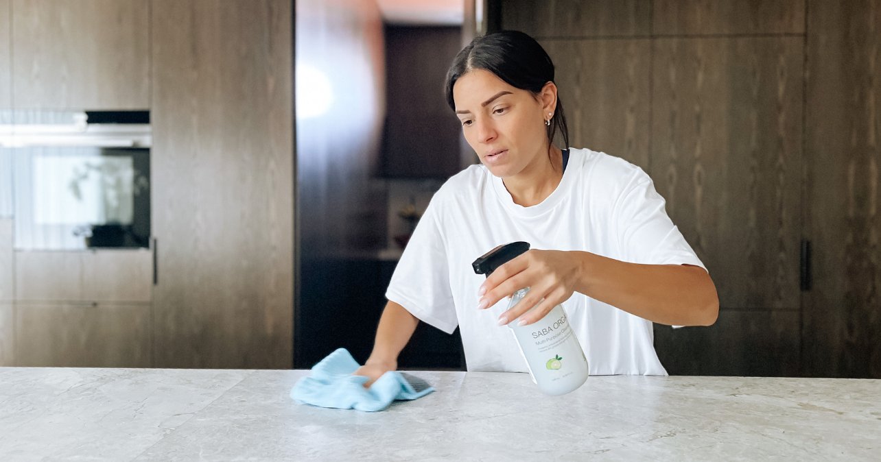 person using spray and wipe on marble bench top